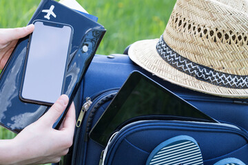 Summer, tourism. Blue suitcase collected for travel. Female hands holding passport, tickets and phone. Free space on the phone screen.
