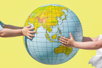 Children's hands holding a ball in the shape of the Earth, yellow background.