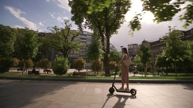 Pretty young woman riding an electric scooter on a street