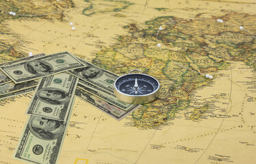 American dollars in form of arrow that indicates direction and navigation compass on old vintage world map as symbol of tourism with compass, travel with compass and outdoor activities with compass