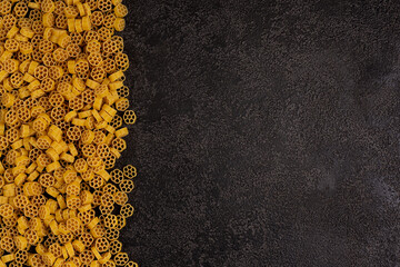 A pile of raw yellow pasta, isolated against a dark structural background with space to copy. top view