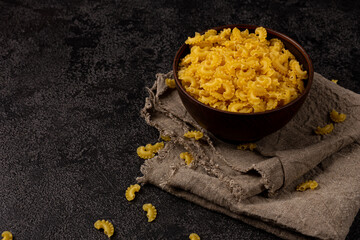 Burlap napkin on a dark structural background, top view. It has raw macaroni in a black bowl
