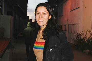 portrait of young woman smiling happy with queer lgbtqia+ pride flag on sweater at night outdoors with flash  - obrazy, fototapety, plakaty