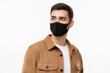 Young man in brown cargo shirt and black face mask looking away, isolated on gray background