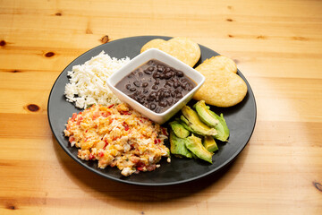 Typical Venezuelan breakfast scrambled eggs with tomato called Perico, black beans, hard white cheese, arepas and avocado.