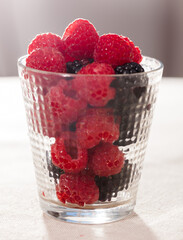handful of fresh raspberry and blackberry berries in glass on white background