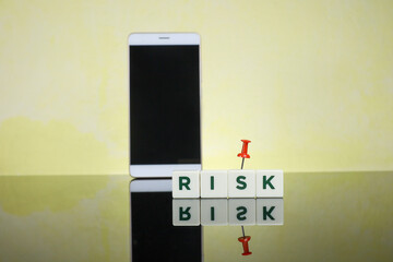 Risk and technology concept.  Text on Risk written on the white cubes with a smartphone at the back creating a blur effect