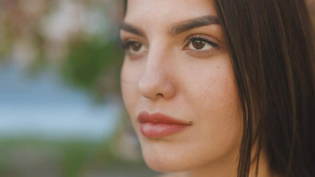 Close up Face serious attractive woman stand outdoor relax. Beautiful around brown eyes. Beautiful woman with natural make-up in cherry blossom forest. Super slow motion in 4k