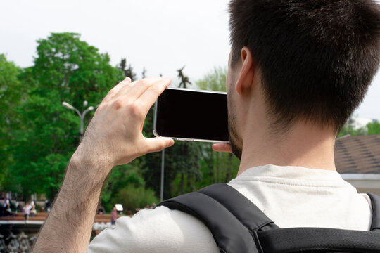 A young man takes pictures on his phone in the park.