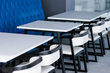 Black and white chairs and tables on a food court against a blue wall. Cafe interior. High quality photo