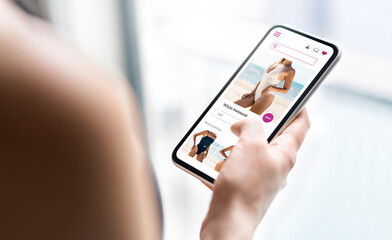 Online shop website in phone. Fashion store product page in smartphone. Woman looking for swimsuit sale. Web site mockup. Ecommerce and retail business concept. Customer buying and ordering apparel.