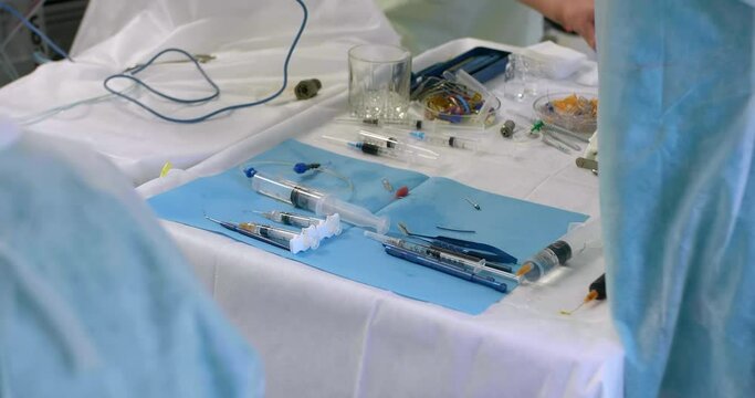 Table with surgical instruments during surgery in operating room. Nurse hands touching surgical instrument on table during surgical operation in medical clinic.