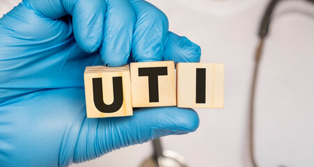 UTI Urinary tract infection - word from wooden blocks with letters holding by a doctor's hands in medical protective gloves. Medical concept.