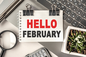 HELLO FEBRUARY text on a notepad and laptop, office tools. Business, financial concept. remote training. Coffee break, ideas, notes, goals or writing a plan, invitation concept. Top view, flat lay.