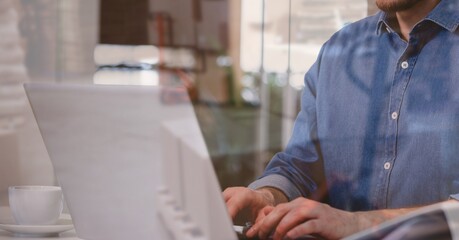 Composition of man using laptop over stacked up shelves with boxes in warehouse