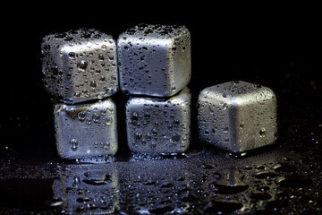 Stainless steel cubes simulating ice for cooling drinks on a black surface with a reflection.