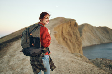 happy traveler woman resting in the mountains near the sea and back view of a model backpack
