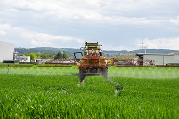 Spraying a crop field with a tractor that has a tank with spray nozzles.