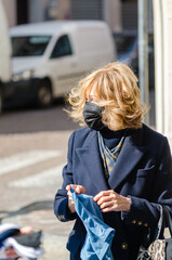 Elegant caucasian woman with a face mask choosing clothes at the street market