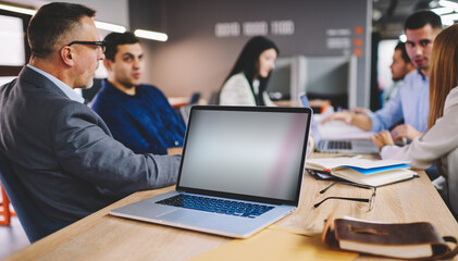 Selective focus on mockup laptop computer with copy space area for financial internet advertising, group of male and female colleagues discussing blank technology during working day in office