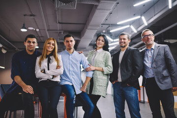 Fototapeta premium Happy male and female colleagues dressed in smart casual and formal clothes smiling at camera during team building brainstorming in office interior, successful business partners posing togetherness