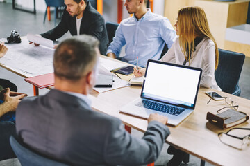 Male employer using blank laptop computer with copy space area during collaboration brainstorming with colleagues, businessman browsing web information on mockup netbook technology while building team