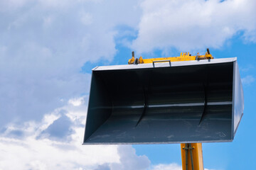Bucket of loader on a blue sky background. Footprints on the surface. Industrial background. Banner wallpaper. Heavy machinery rental concept. Copy space.  © Ganna Zelinska