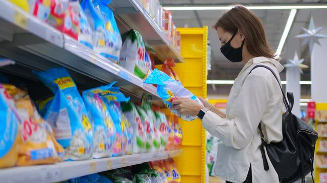 young housewife with face mask is choosing washing powder in supermarket