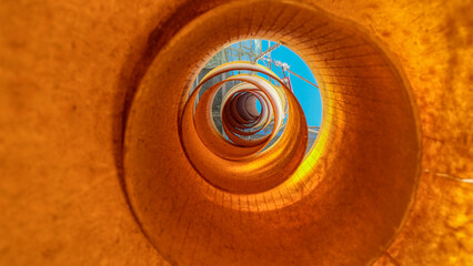 Fototapeta na wymiar View from the inside of construction yellow plastic garbage chute. Above you can see the blue sky
