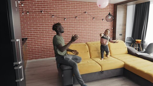 African-American father playing with little boy, throwing balloon to each other