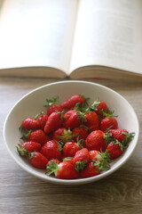 Bowl of strawberries and open book on a table. Selective focus.