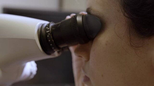 Female scientist or gemologist looking through a microscope to examine diamond. Gem or diamond lab or hospital nurse or doctor uses professional device to see up close and inspect an object in macro