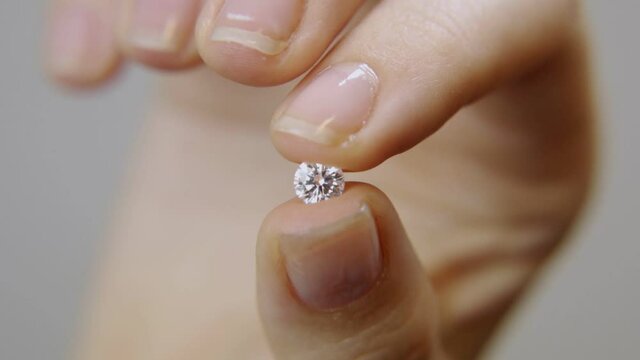 Macro close up on a female hand holding round shape diamond in fingers. Showing the shiny and expensive classic stone. Luxury jewelry store. Original or lab-made diamonds held in woman's hand