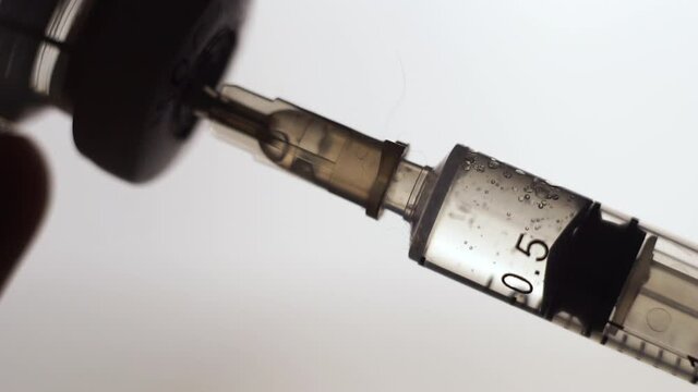 vaccination concept, drawing clear liquid into a syringe close up. bubbles inside the syringein. soft grey background. horizontal slow motion macro HD video.