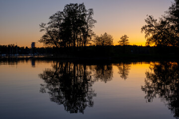 Fototapeta premium A beautiful silhouette of a large tree on an island casting reflection on the water during sunset.