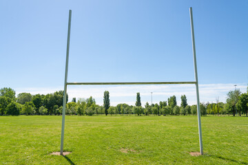 Fototapeta na wymiar Isolated rugby goal post in a pitch of a park in Milan, Italy. Green field and green trees. Blue sky on the background.