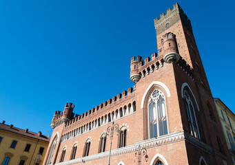 The famous tower in the centre of Asti, Italy, named "Torre Comentina" and its beautiful palace made of red bricks. Blue sky on the background.