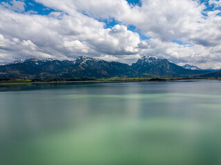 Naklejka premium Forggensee Allgäu from above - Aerial view with mirroring clouds on a sunny day at the feet of the alps close to Füssen and Neuschwanstein