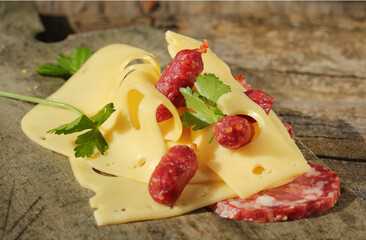 Сlose-up of small servelat sausages and slices of maasdam cheese on a wooden background