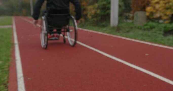 Anonymous Paralympian man with defective legs rides in a wheelchair on the street of the stadium outside dressed in sportswear