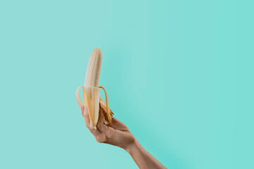 Closeup a woman's hand holding a ripe banana isolated on green pastel colors background