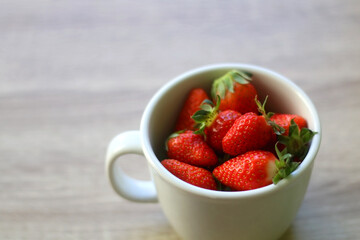 Mug filled with fresh strawberries on wooden table. Selective focus.