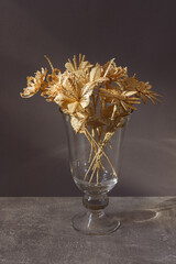 A glass vase with a bouquet of flowers made from straw on gray background