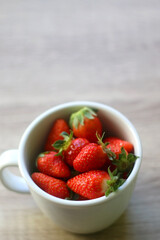 Mug filled with fresh strawberries on wooden table. Selective focus.
