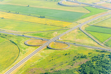 Cloverleaf interchange seen from above. Aerial view of highway road junction in the countryside with trees and cultivated fields. Bird's eye