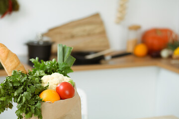 Interior of kitchen room with wooden table, big window and a paper bag full of fresh foods ready to cook. Template.
