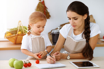 Happy woman and her daughter are searching for new recipes for a family feasting, sunny kitchen. Christmas, New year, Thanksgiving, Anniversary, Mothers Day. Healthy meal cooking concept