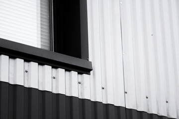Black and white corrugated iron sheet used as a facade of a warehouse or factory with a window. Texture of a seamless corrugated zinc sheet metal aluminum facade. Architecture. Metal texture.
