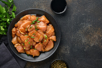 Raw chicken meat marinated in teriyaki soy sauce, onions and pepper in a black plate on a dark slate, stone or concrete background. Top view with copy space.