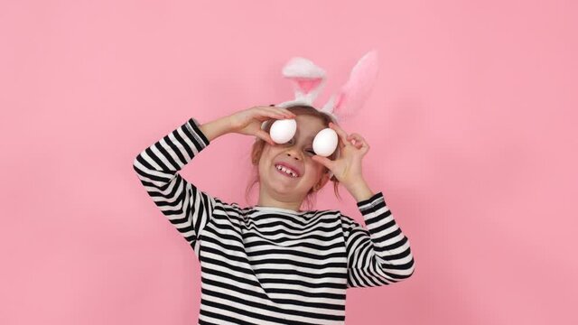 Little girl with bunny ears is having fun and playing with Easter eggs of different colors. Fun at Easter. High quality 4k footage.